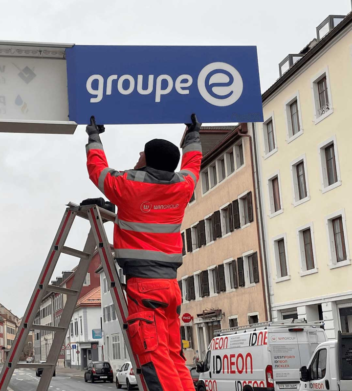 Un collaborateur installe l'enseigne Groupe E sur le mur d'une succursale neuchâteloise