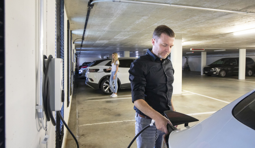 Homme rechargeant une voiture électrique dans un parking illustrant les solutions d'achat et de location de bornes électriques proposées par Groupe E pour les professionnels