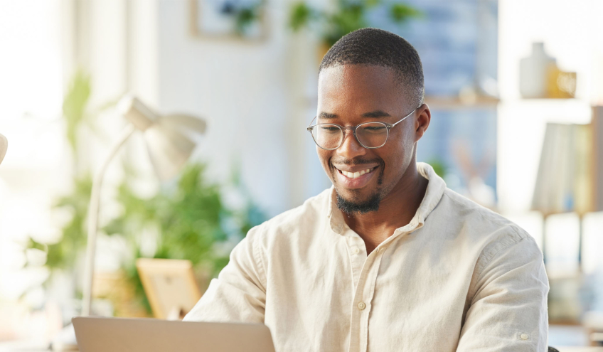 Un homme souriant travaille sur son ordinateur dans un environnement lumineux et accueillant, représentant les avantages de l'offre Électricité Bonus de Groupe E pour les particuliers