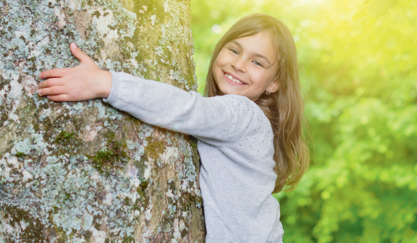 Ein lächelndes Mädchen umarmt einen Baum und symbolisiert das Engagement von Groupe E für nachhaltigen und umweltfreundlichen Strom für Privatkunden