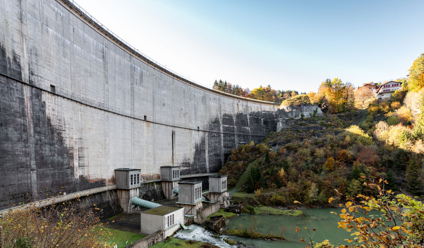 Ansicht eines Wasserkraftwerksdamms, umgeben von herbstlicher Natur, der die Expertise von Groupe E im Bereich Wasserkraft und seine spezialisierten Schulungen veranschaulicht