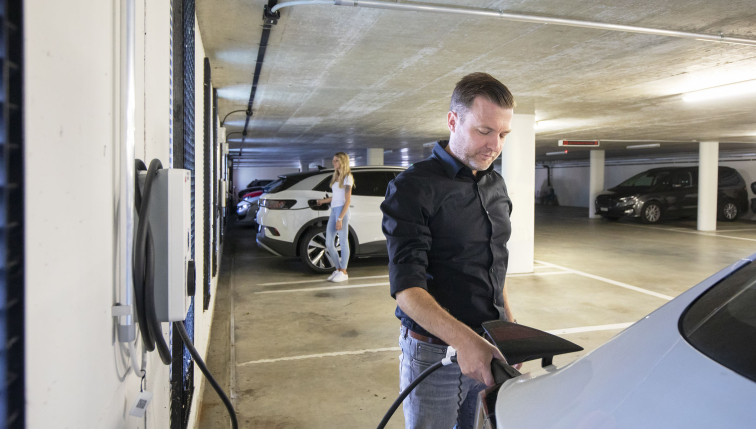 Mann lädt ein Elektroauto in einer Tiefgarage auf, mit einer Frau im Hintergrund, als Darstellung der Kauf- und Mietlösungen für Ladestationen von Groupe E für Fachleute