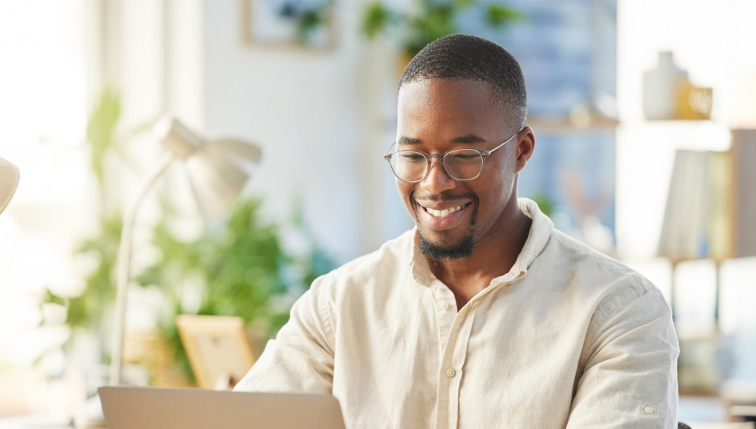 Un homme souriant travaille sur son ordinateur dans un environnement lumineux et accueillant, représentant les avantages de l'offre Électricité Bonus de Groupe E pour les particuliers