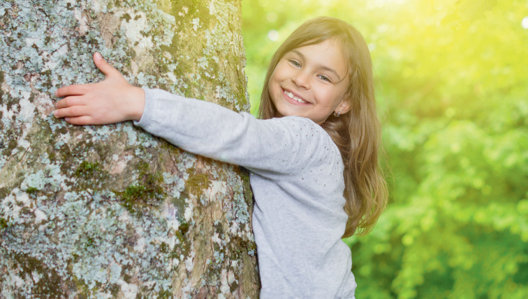 Ein lächelndes Mädchen umarmt einen Baum und symbolisiert das Engagement von Groupe E für nachhaltigen und umweltfreundlichen Strom für Privatkunden