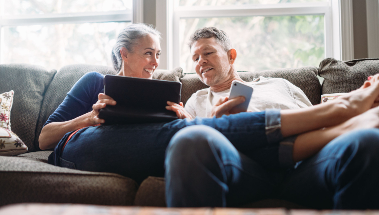 Un couple détendu à la maison, consultant une tablette et un smartphone, illustrant la simplicité et l'accessibilité des solutions de facturation de chauffage à distance proposées par Groupe E pour les clients privés