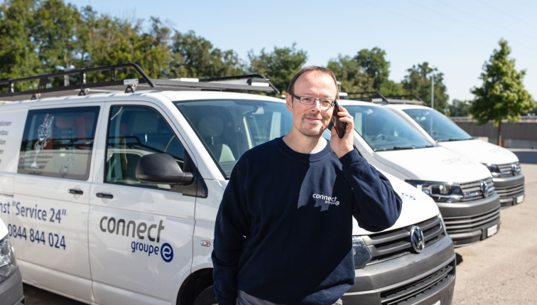 Technicien de Groupe E en communication près d'un véhicule de service, illustrant le service de maintenance pour pompes à chaleur destiné aux professionnels